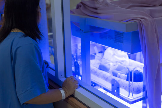 Mother Watching At The Newborn Baby With Hyperbilirubinemia / Neonatal Jaundice Under Blue UV Light For Phototheraphy On Infant Warmer In Neonatal Intensive Care Unit