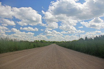 Summer background. White clouds on a blue sky and a road from gravel that goes into the distance