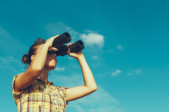Beautiful Young Girl Looking Through Binoculars On Blue Sky Background. Travel Holidays Journey Concept