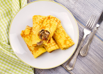 Wrapped thin pancakes  filled with mushrooms on white plate. View from above, top studio shot, horizontal