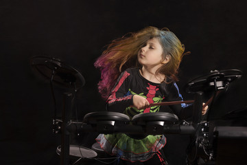 Fototapeta na wymiar Little caucasian girl drummer with multicolored hair playing the electronic drum kit