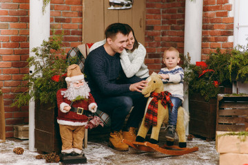 Young happy parents with a cute little child boy on rocking horse, dressed in sweater in decorated New Year room with Santa at home. Christmas good mood. Lifestyle, family and holiday 2018 concept