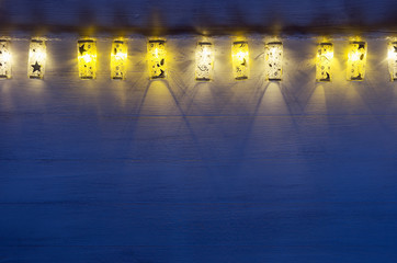 Christmas lights lanterns burn on blue ultramarine wooden background. New Year festive home interior.