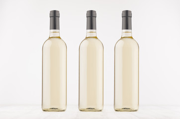 Three transparent wine bottles with white wine on white wooden board, mock up. Template for advertising, design, branding identity.