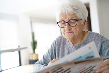 Portrait of old woman reading newspaper at home