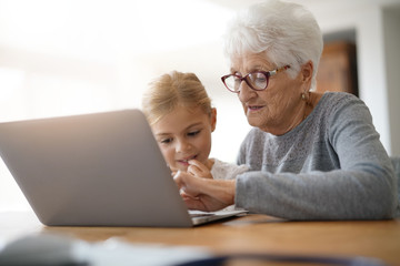 Little girl with grandmother using laptop computer - obrazy, fototapety, plakaty