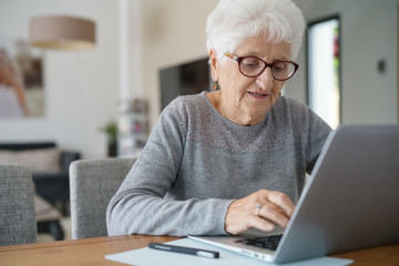Fototapeta na wymiar Old woman at home using laptop computer