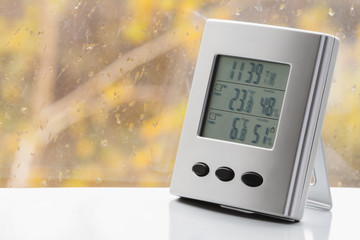 Weather station device with weather conditions inside and outside. Background of a window with...