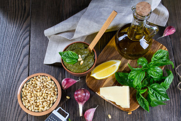 Tradizione Italiana Homemade Pesto recipe ingredients on dark table. Parmesan cheese, basil leaves, pine nuts, olive oil, garlic.
