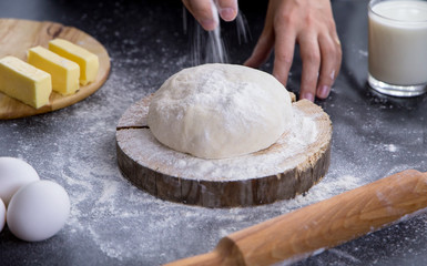 woman sprinkling flour over fresh dough on kitchen table