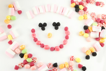 Many sweet candies and marshmallows in face shape on white surface, top view