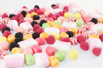 Many sweet candies and marshmallows on white surface, closeup