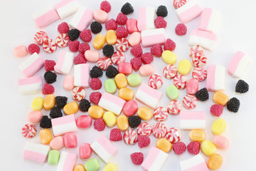 Many sweet and bright candies and marshmallows on white surface