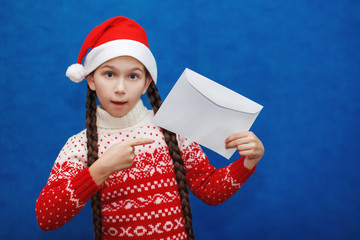 Beautiful girl wearing hat of Santa Claus holding a letter envelope on blue background