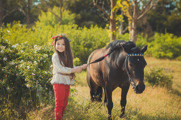 Girl with brunette hair and brown eyes stylish dressed wearing rustic village clothes white shirt and red pants on belt posing with black young horse pony