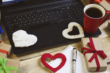  Laptop, a cup of coffee, gifts and handmade hearts, a notebook and a pen. Preparing for Valentine's Day