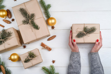 Christmas gift wrapping background, copy space. Female hands holding christmas present box wrapped in kraft, top view. Winter holidays concept, flat lay. Woman with red manicure packing Christmas gift