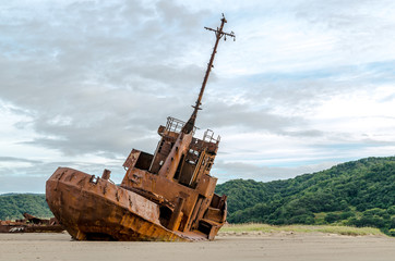 Fototapeta na wymiar Old abandoned ship, standing on the sandy beach in cloudy weather.