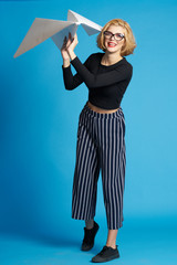 Fototapeta premium woman in glasses with a big paper airplane on a blue background smiling