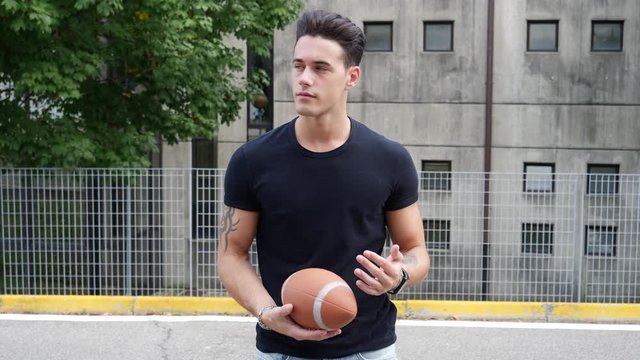 Handsome young man standing on street and holding American football ball.