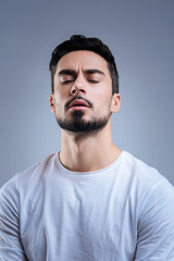 Emotional moment. Expressive young handsome man sitting with his eyes closed and looking impressed while hearing his favorite song