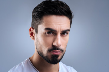 Obraz premium Calmness. Handsome young man having a gorgeous black beard sitting calmly and frowning while being against the blue background