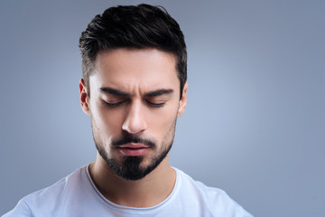 Fototapeta premium Calm. Relaxed kind handsome man sitting with his eyes closed and meditating while being home alone and trying to forget about his troubles