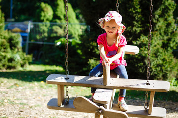 A cute young girl riding a chain carousel swing. Girl puts her hand like a plane's wings.