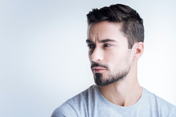 Look away. Calm handsome bearded man looking not pleased with his working day while sitting against the blue background with his head turned right