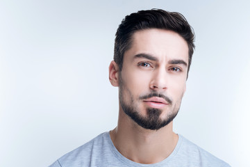 Rather calm. Handsome thoughtful young man feeling calm while sitting against the blue background and slightly frowning