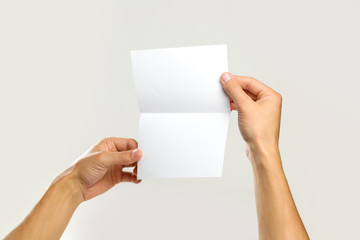 Obraz premium Male hands holding a white sheet of paper. Isolated on gray background. Closeup