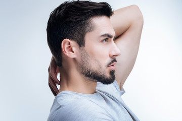 Obraz premium New haircut. Handsome fashionable young man standing against the blue background with his hand on his neck while boasting his new haircut