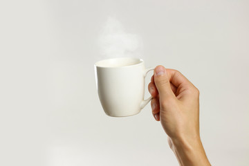 Male hand holding white empty glass mug. Isolated on gray background. Closeup.