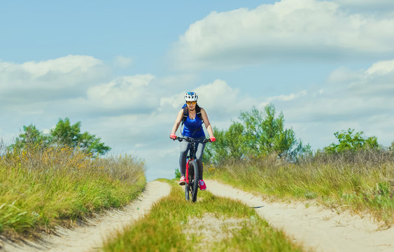 One young woman - an athlete in a helmet riding a mountain bike outside the city, on the road on a summer day.