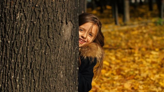 Happy little girl hiding behind the tree