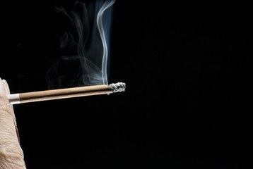 smoking brown cigarette or cigarillus in wrinkled fingers on black background closeup
