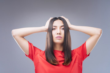 Unhappy. Emotional elegant smart woman standing against the blue background with her hands on her head and feeling sad and lonely