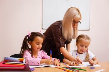 two happy little schoolgirls study in class, the teacher explains