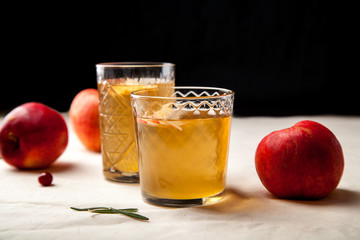 Two vintage glasses with apple cider on black background. Christmas beverages concept. Two red apples and rosemary sprig aside.  Warm backlight. Vertical composition.