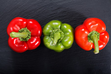 Organic red and green bell pepper on black slate stone plate with copy space