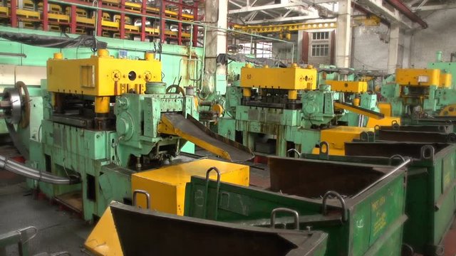 A professional view of some metal circular items which roll down from a forging press into some metal box in a workshop at a plant. The workshop looks spacious, modern and big
