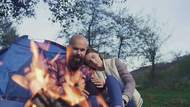 A young couple of hippesters sit at hte fire in a tent town