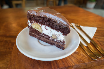 Chocolate Fudge with white cream and banana on white plate on wooden table. Eat chocolate cake in a relaxing time at the coffee shop