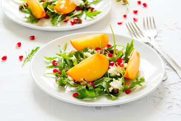 Fresh autumn salad with persimmon, arugula, cheese and pomegranate seeds on white table cloth. Space for copy