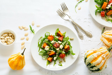 Fresh autumn salad with baked pumpkin, arugula, cheese and seeds on white table cloth. Space for copy