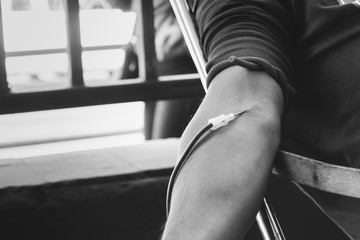 close up on arm of blood donor while donating blood on black and white tone