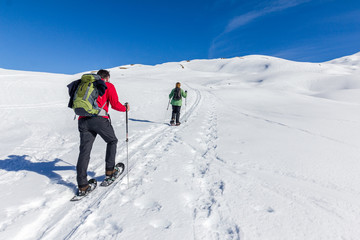 Fototapeta na wymiar Couple is snowshoe hiking in alpine winter mountains. Bavaria, Germany.