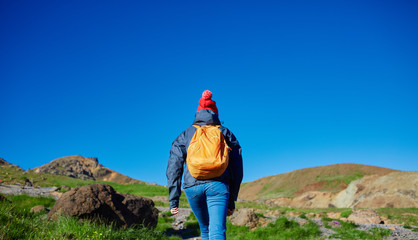 Naklejka premium back view of woman traveler on a walk in the Valley of the river of Hveragerdi Iceland. Hiking Tour of Reykjadalur Hot Springs