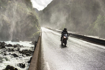 Motorbike driving fast on wet canyon valley road and bridge across river.