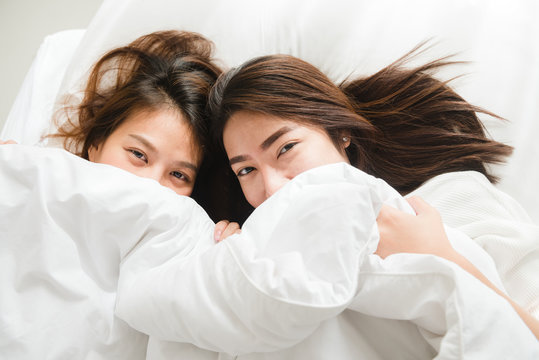 Top view of beautiful young asian women lesbian happy couple showing surprise and looking at camera while lying in bed under blanket. Funny women after wake up. Lesbian couple together indoors concept